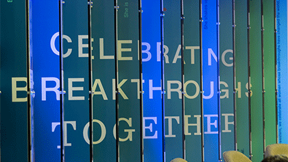 A wall of blue and green slats, possibly vertical blinds. Written across the slats: celebrating breakthroughs together