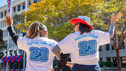 Backs of two women standing outside wearing matching jerseys, that say Charitable Campaign 23.