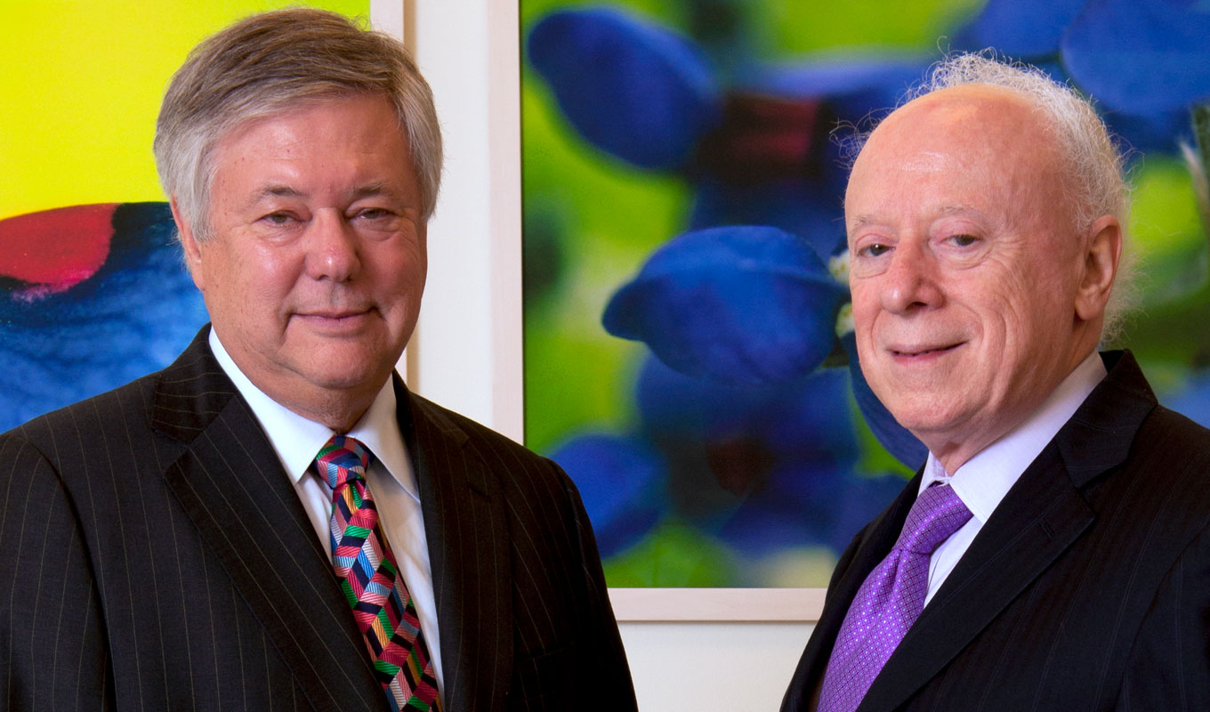 two men in dark suits in front of colorful paintings