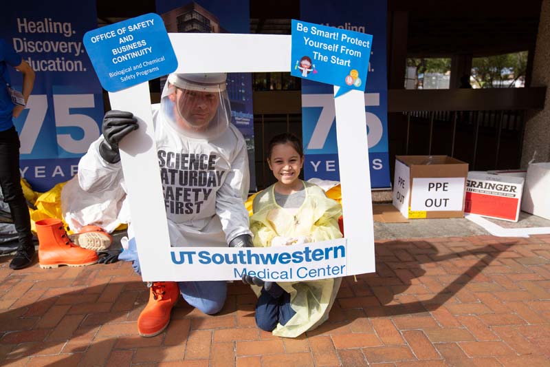 Patrick Conley, Director of Biological and Chemical Safety in the Office of Safety and Business Continuity, take pictures with visitors dressed in personal protection equipment.