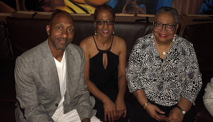 Three people, an older woman next to an adult man and woman, sitting next to each other and smiling