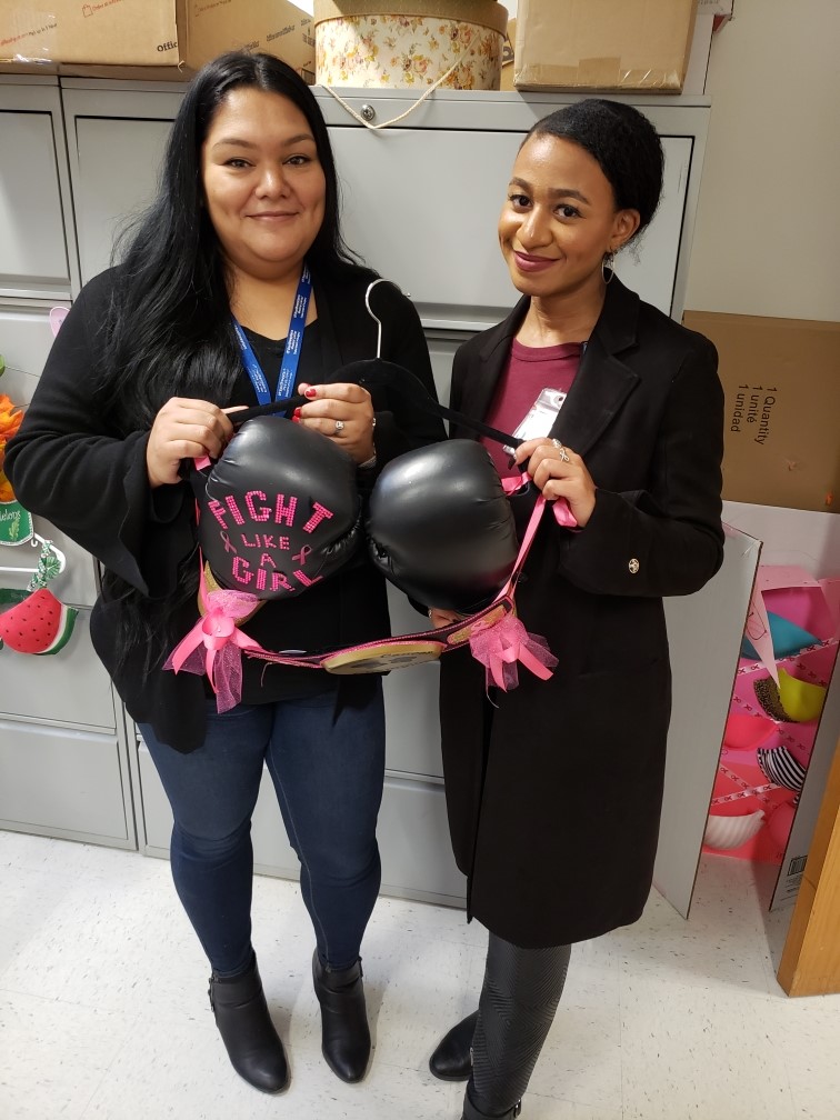 Two women holding a bra made of boxing gloves with pink writing
