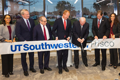 Group of people holding a large ribbon and cutting it in the middle