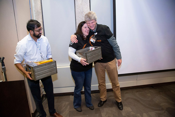 Man hugging a woman holding a crate, and another man standing next to them holding a crate