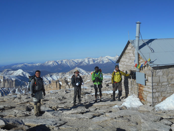 Four men standing next to a cabin on a mountain top