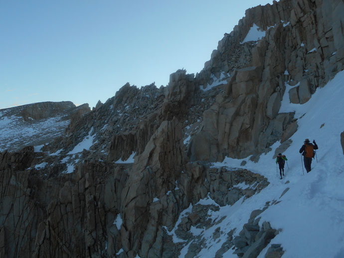 Two people hiking in the snow along a steep mountain face