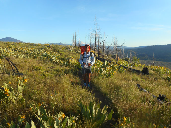 Eric wearing a backpack in a field with mountains in the back