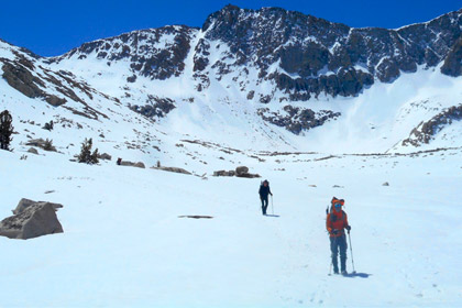 Two people hiking in snow with a beautiful mountain range behind them