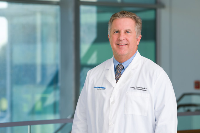 Man with lab coat, greying hair, standing in front of windows