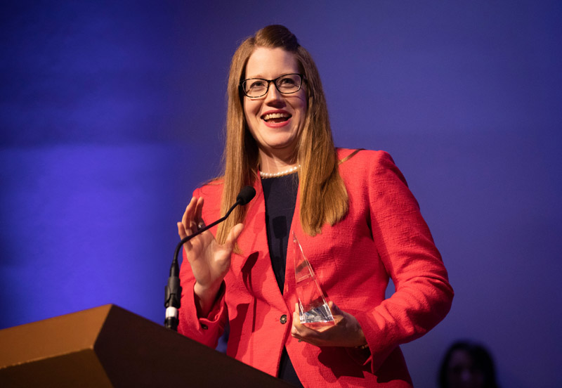 Woman in red blazer holding glass award and smiling