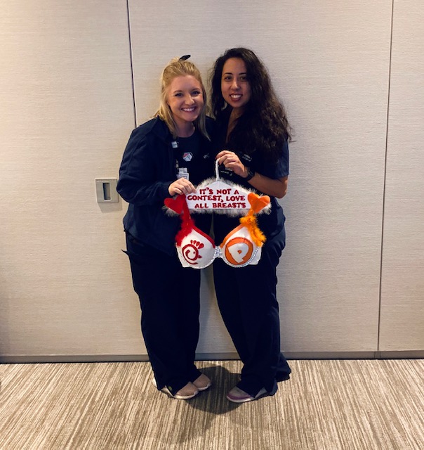 Two women holding a bra decorated with the chick-fil-a and popeyes logos