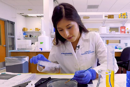 female student in white lab coat performs experiment