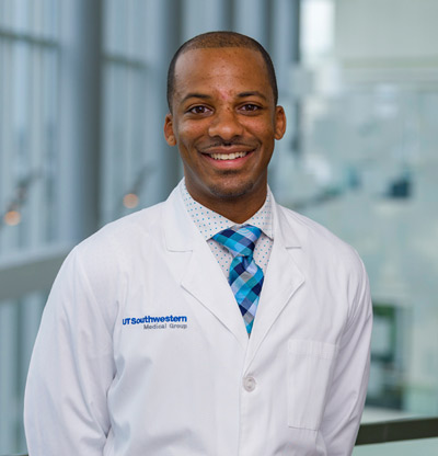 Man with short cropped hair in white coat, blue tie, smiling