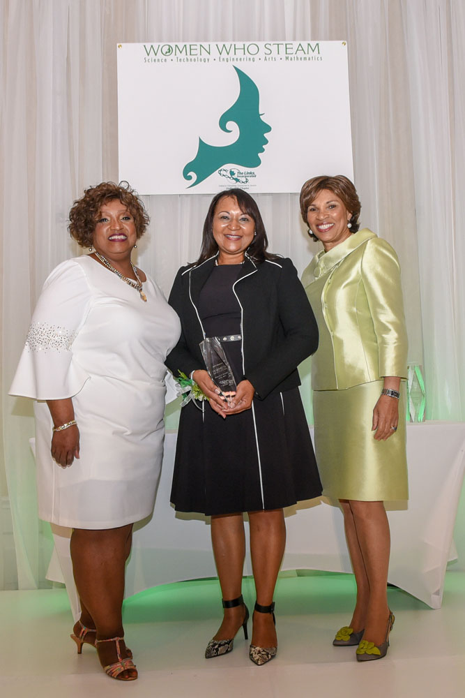 Three women standing in front of a sign that says Women who STEAM