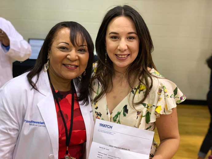 Woman wtih lab coat on standing next to another woman holdling a letter up to the camera