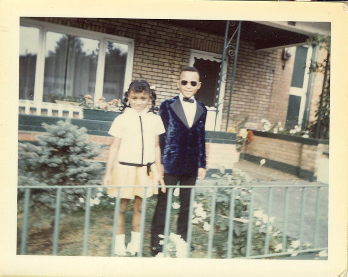 Older photo of young boy and girl standing next to each other in front of a house