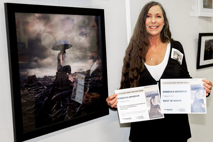 Woman holding certificate while standing next to her framed photography work