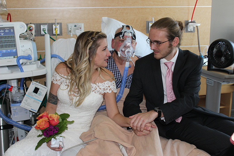 Father, Bride, and Groom sit together on bed as vow are recited