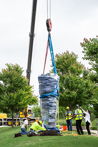 Workers with crane installing Dumna sculpture on plaza