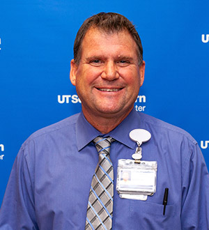 Man with short brown hair, blue dress shirt and tie, smiling