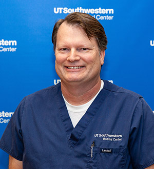 Man with parted brown hair wearing dark blue UTSW scrubs