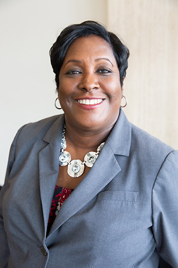 Woman with short dark hair, hoop earrings, light gray blazer