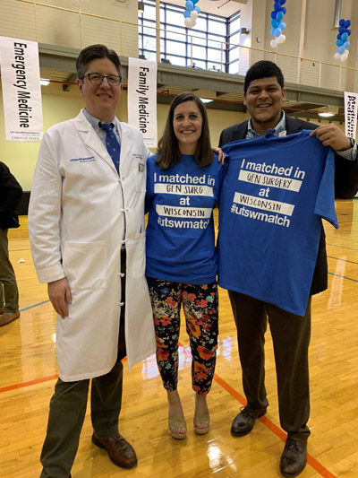 Man in white lab coat standing next to man and woman with blue shirts stating where they matched
