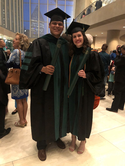 Man and woman in graduation gowns holding green tubes