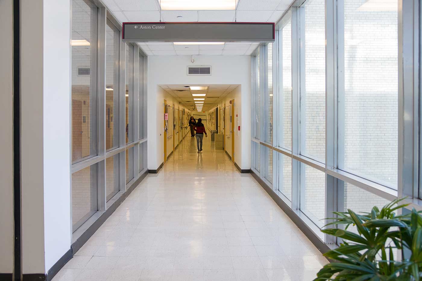 Long hallway with person walking down it, lined by windows