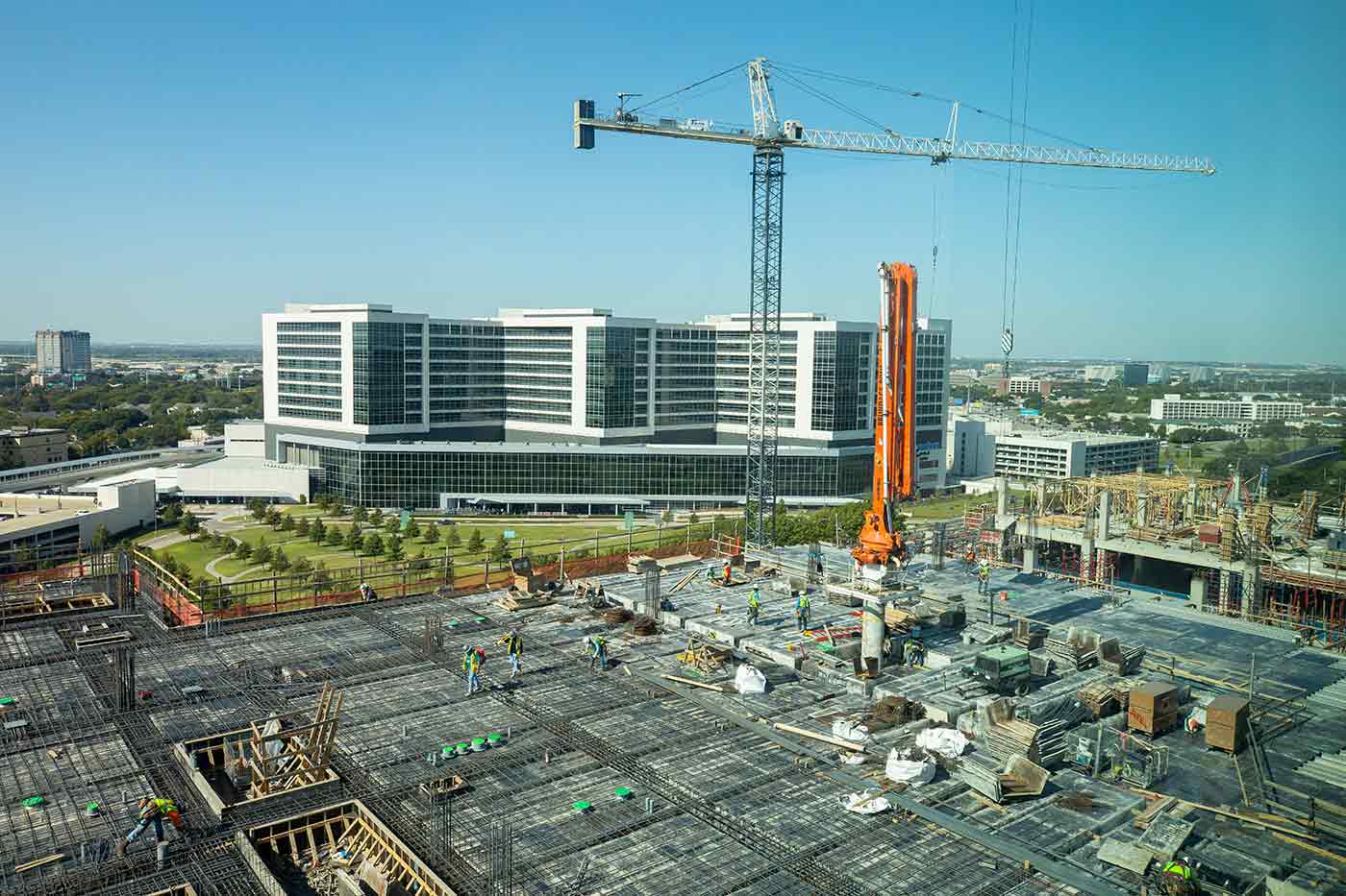 Workers on a building walking on rebar, with construction crane and large building in background