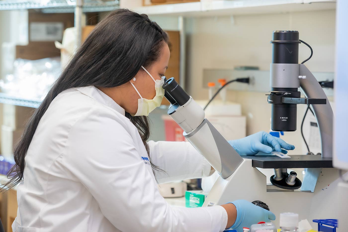 Woman in lab coat looking into microscope.