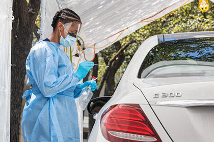 Woman in mask, face shield, and gown taking sample by car