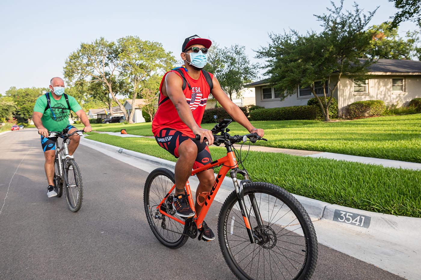 Two men on bicycles next to green lawns