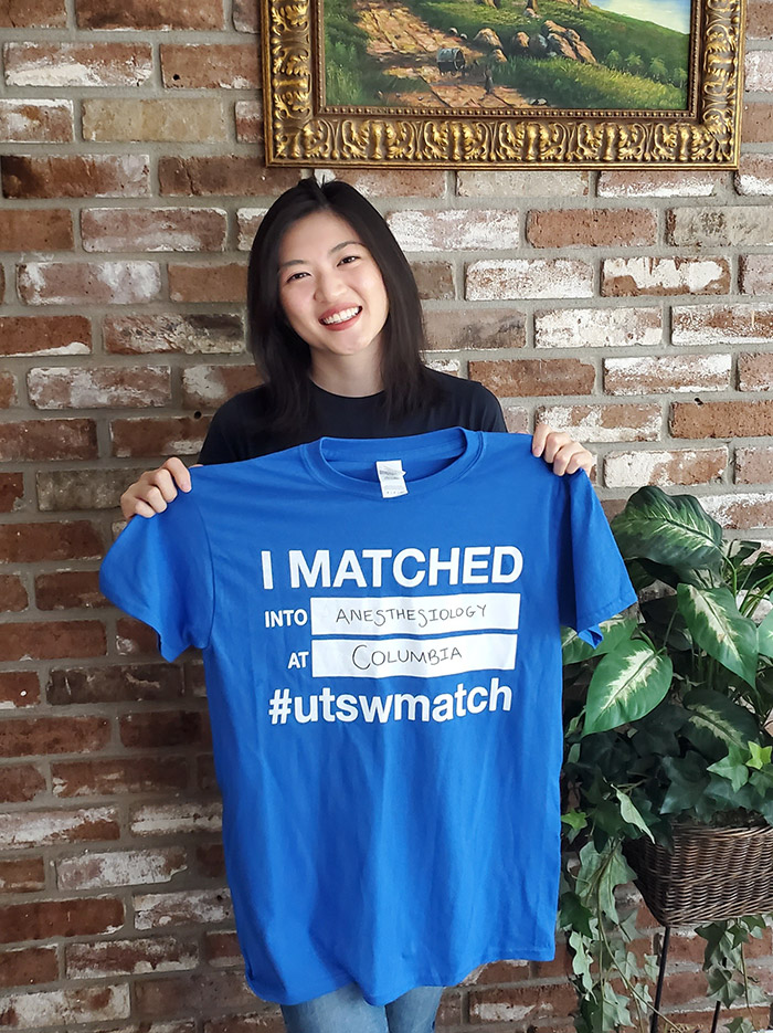 Woman smiling and holding blue shirt that announces matching in anesthesiology at Columbia