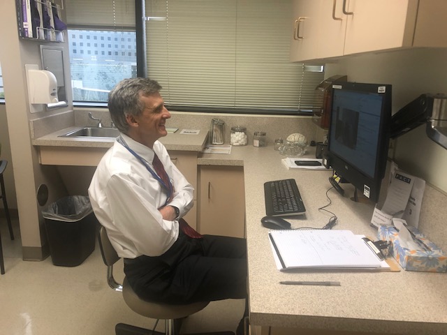 Man in white shirt, smiling and leaning back while talking into computer