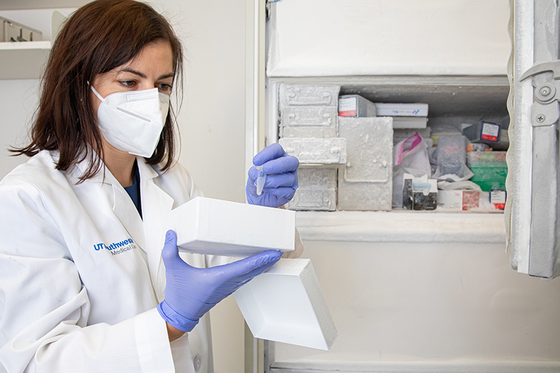 Woman in white coat, mask, and gloves works with equipment