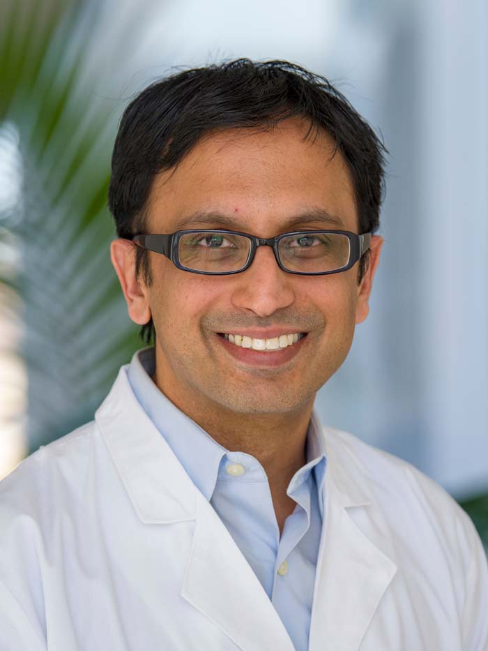 Man with dark hair, glasses, wearing white lab coat