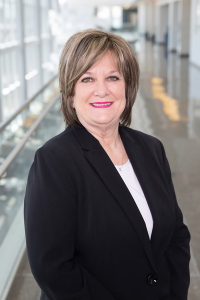 Woman with short grey hair, wearing black jacket and white shirt