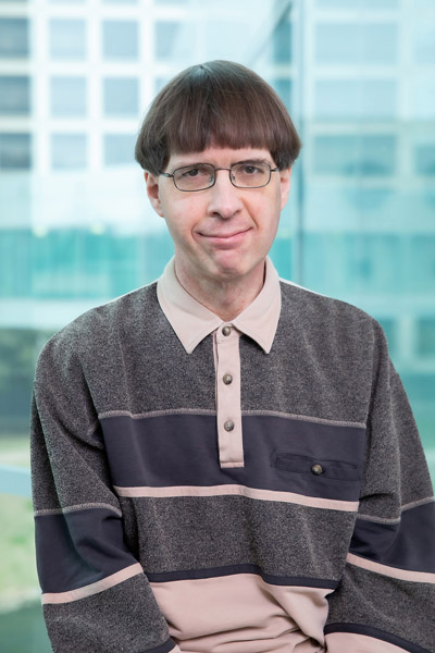 Man with brown hair, wearing grey shirt and black glasses