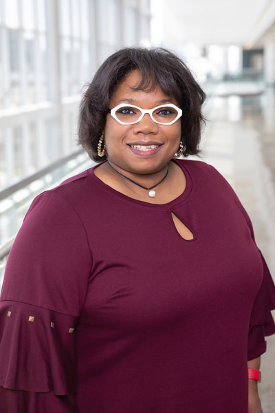 Woman with black hair, wearing burgundy top and white glasses