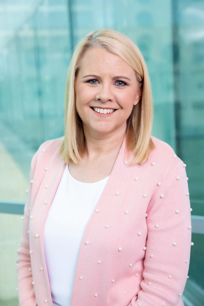 Woman with blonde hair, wearing pink jacket and white shirt