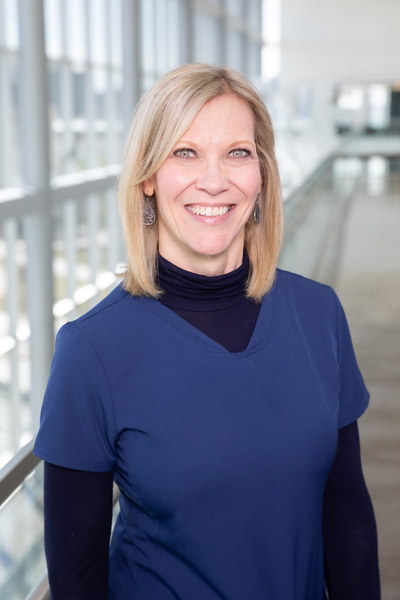 Woman with blonde hair, wearing blue scrubs and black undershirt