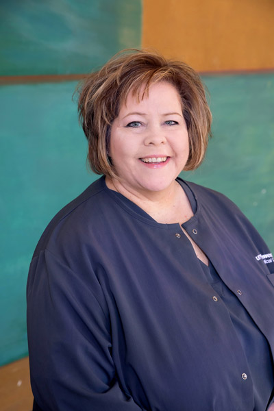 Woman with brown hair, wearing blue scrub top