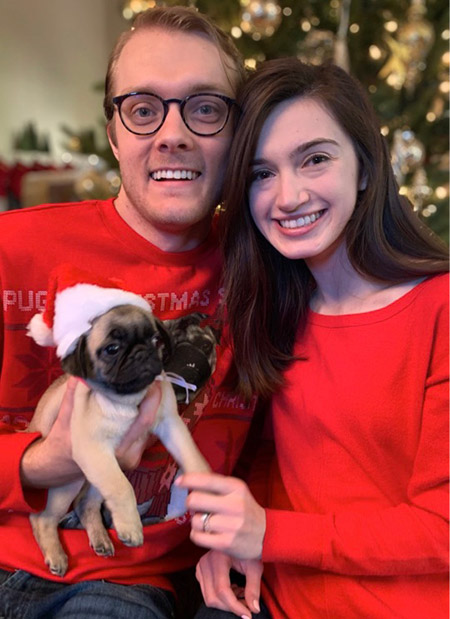 Man and woman wearing Christmas sweaters and holding a small dog