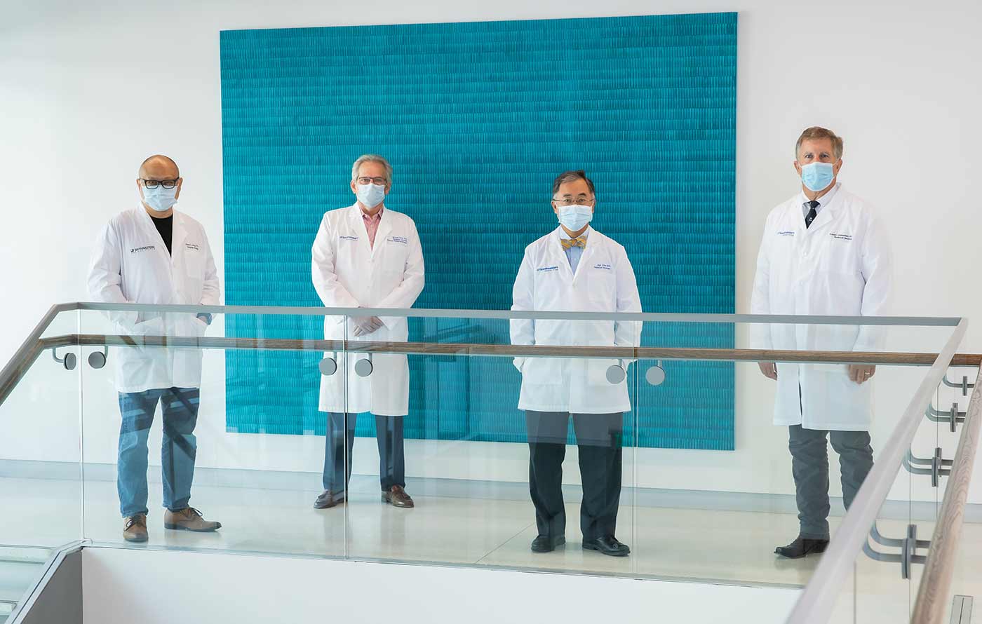 Fourp men in lab coats, wearing masks, spaced apart