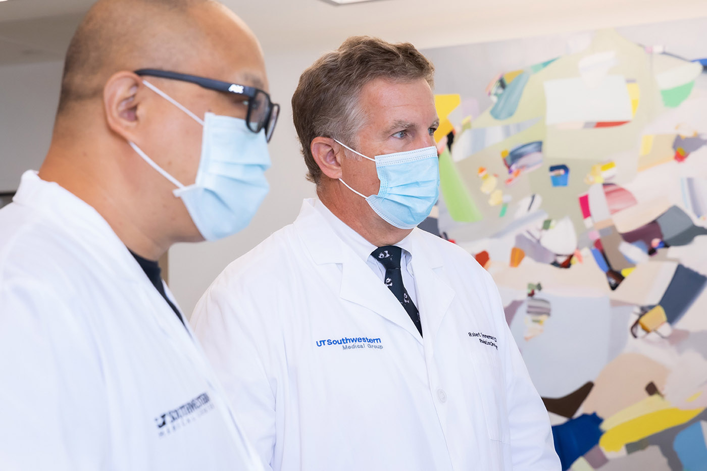 Two men in masks and lab coats looking at screen