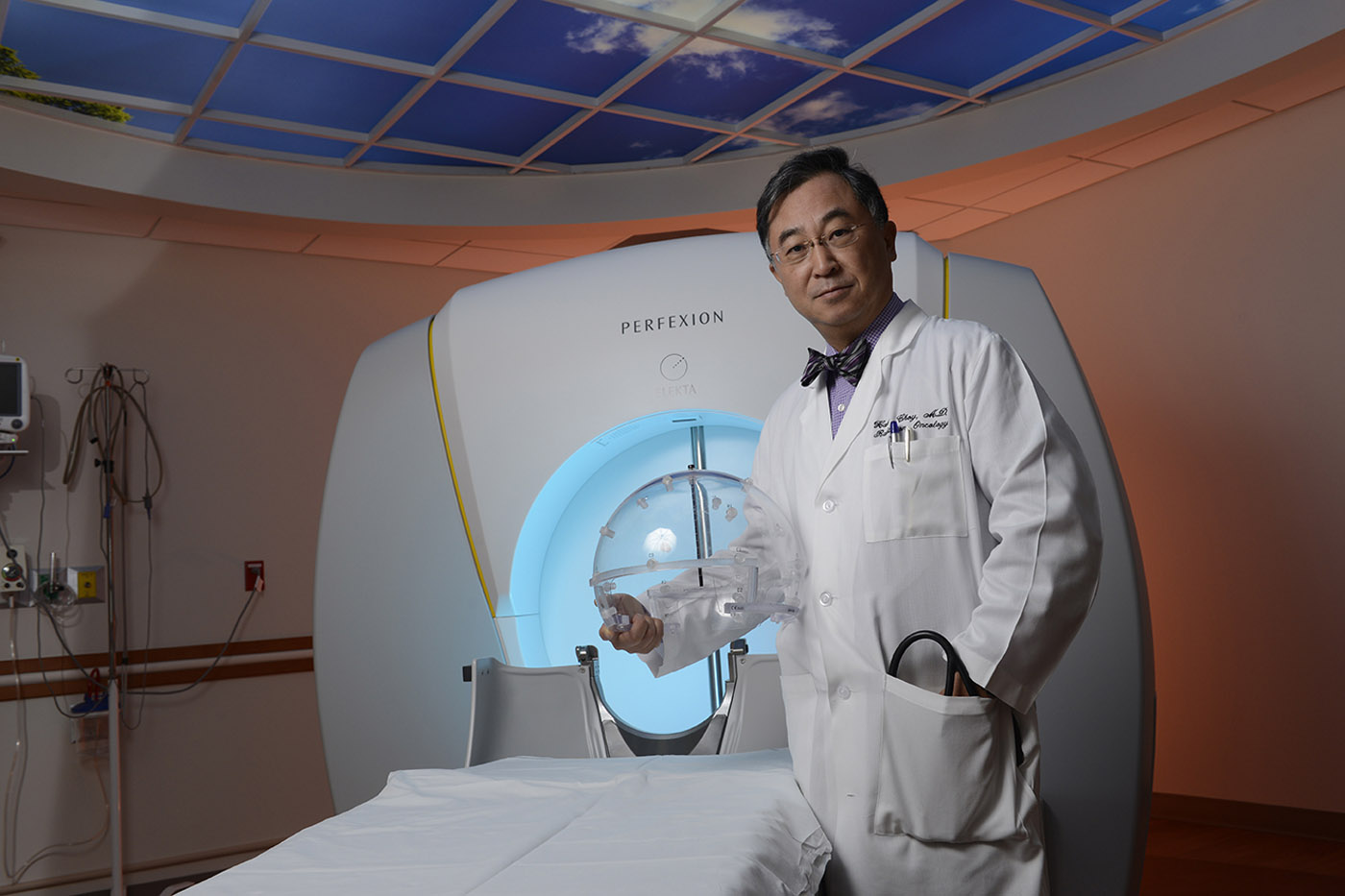 Man in lab coat and bowtie, standing in front of large medical machine