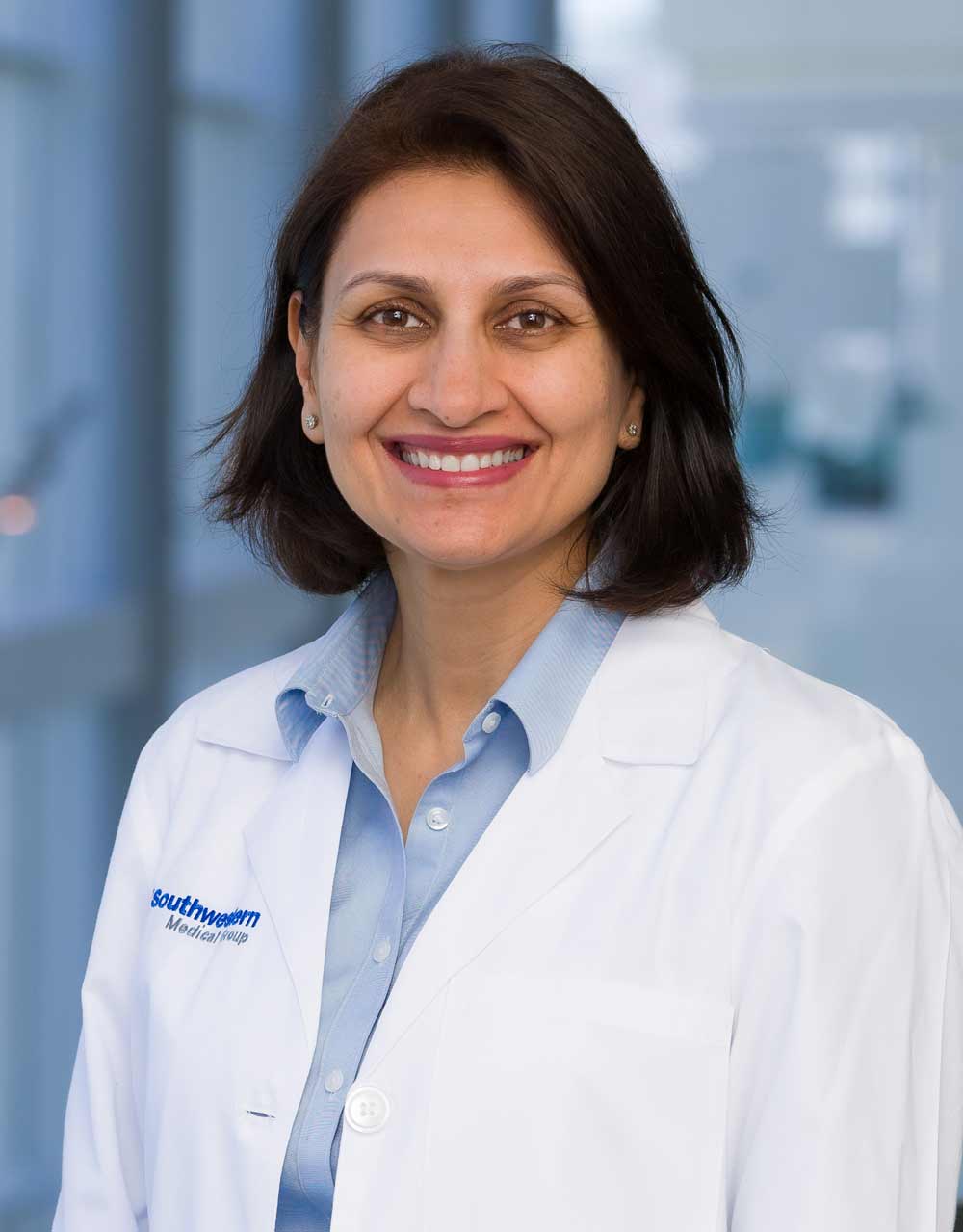 Woman with dark hair, wearing lab coat and light blue shirt