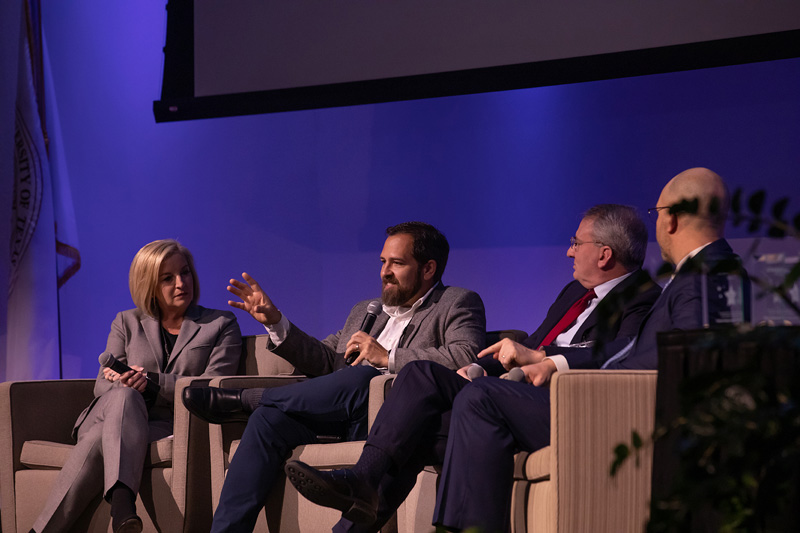 Group of four people sitting on a stage talking into microphones