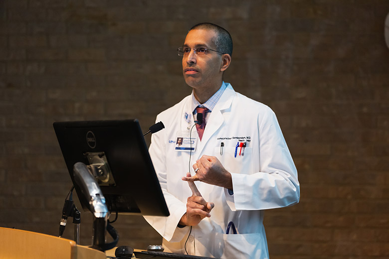 Man in white lab coat speaking at podium